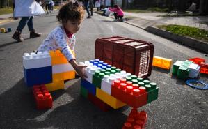 Niños de primaria jugando con juegos didácticos en la calle, acompañados por maestras y familiares
